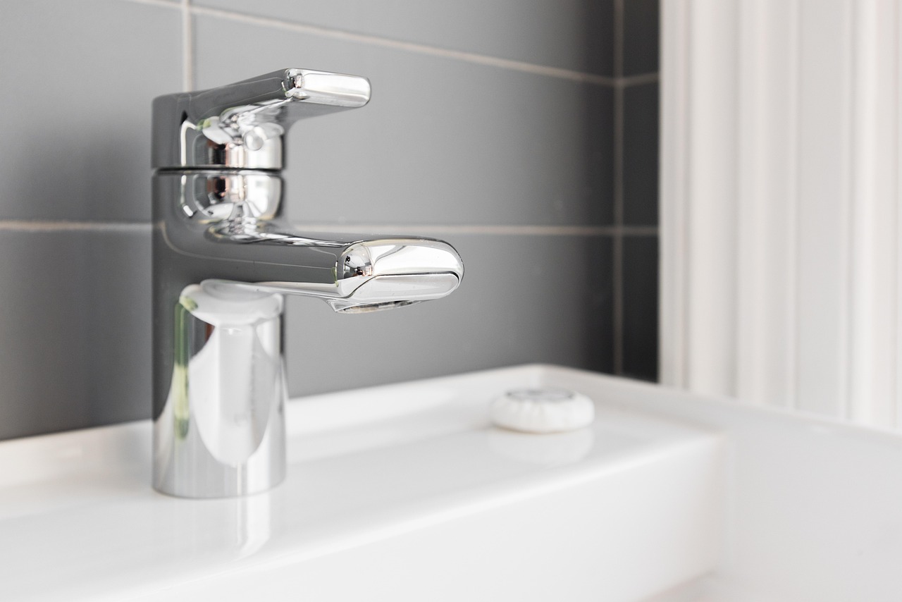 Chrome basin mixer tap on a white sink against a grey tiled wall